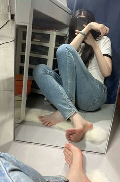 Person in jeans and a white t-shirt sitting on the floor, reflected in a mirror