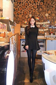 Woman in a black dress with a white collar and tights standing in a cafe