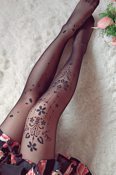 Legs in black tights with floral patterns on a white fur rug
