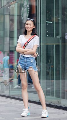Woman in a white t-shirt and distressed denim shorts smiling on a street