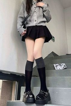 Person in a pleated skirt, cardigan, and knee-high socks on stairs