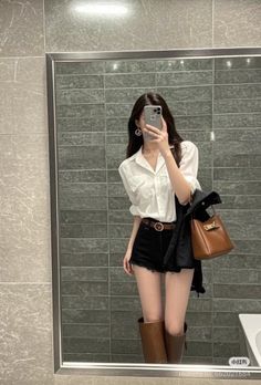 Woman in a white shirt and black shorts taking a mirror selfie