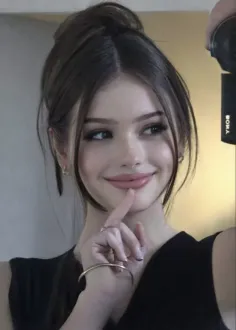 Woman with dark hair in a bun, wearing earrings and a bracelet, smiling