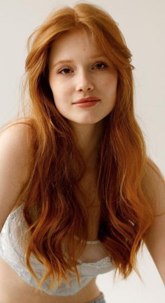 Woman with long red hair wearing a lace bra, looking at the camera