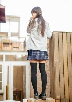 Woman in a plaid skirt and knee high socks looking over her shoulder outdoors