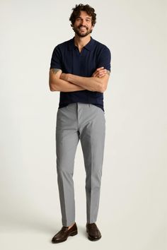 Man in a navy polo shirt and grey pants smiling with arms crossed