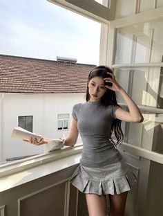 Woman in a grey dress and pleated skirt standing by a window
