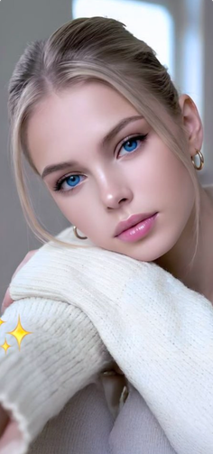 Blonde woman with blue eyes wearing a white sweater and hoop earrings