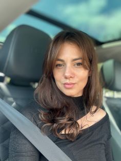 Woman with long brown hair in a car, wearing a black top and seatbelt