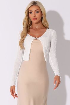 Woman with blonde hair wearing a white shrug and beige dress