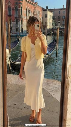 Woman in a slip dress and cardigan taking a mirror selfie by a canal