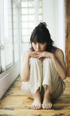 Woman with a messy bun and bangs sitting barefoot on a wooden floor