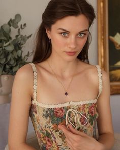 Woman with long hair and green eyes wearing a floral top and jewelry indoors
