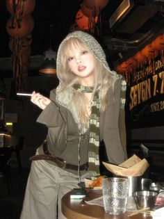 Woman with blonde hair and a hoodie holding a cigarette in a dark indoor setting