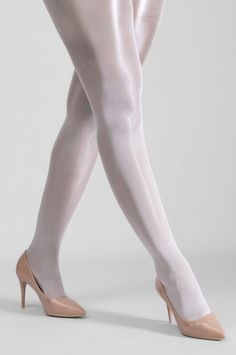 Legs in white tights and nude high heels against a light background