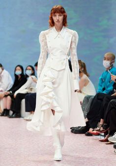 Model in a white ruffled dress with lace sleeves on a runway