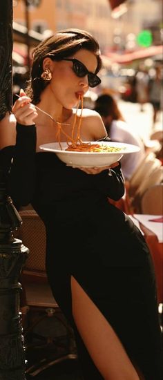 Woman in a black dress and sunglasses eating pasta outdoors