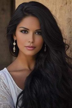 Woman with long black hair and earrings wearing a white top