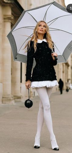 Woman in a black jacket and white tights holding an umbrella outdoors