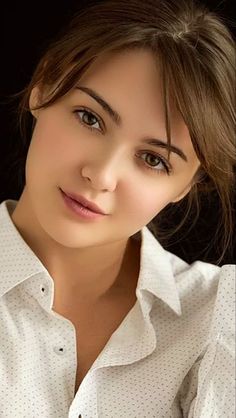 Woman with brown hair wearing a white shirt against a dark background