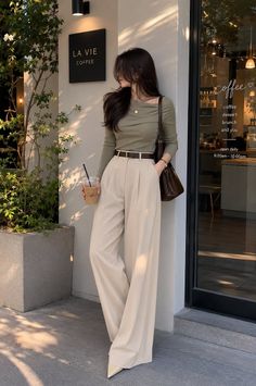 Woman in a green top and wide leg pants holding an iced coffee outside a cafe