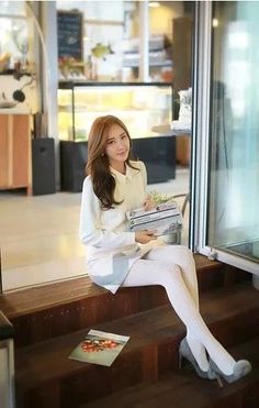 Woman with long hair wearing a white shirt and tights, sitting indoors
