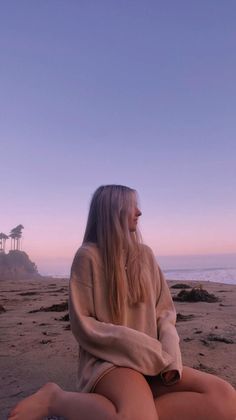 Woman with long blonde hair sitting on a beach at sunset