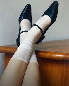 Legs with black shoes and white socks crossed over a wooden surface