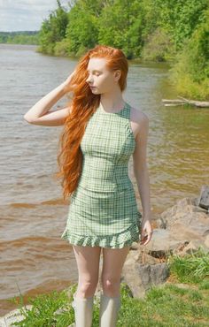 Woman with long red hair in a plaid dress standing by a river