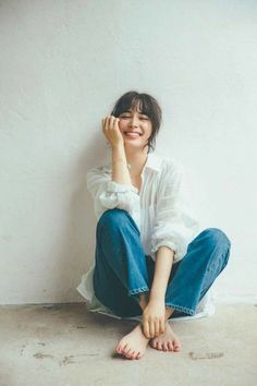 Woman in a white shirt and blue jeans sitting barefoot on the floor