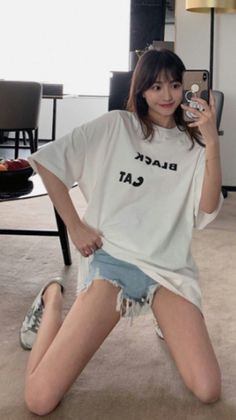 Woman in a white t-shirt and denim shorts taking a mirror selfie