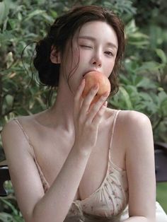 Woman in a floral dress winking and biting a peach with wet skin