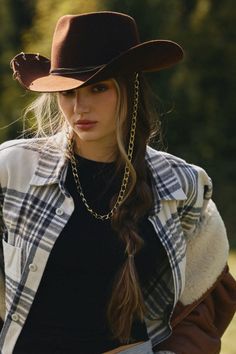Woman in a cowboy hat and plaid shirt with a long braid and gold chain