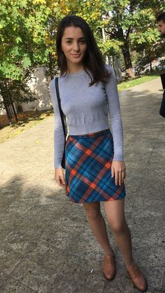 Woman in a grey long sleeve shirt and plaid skirt outdoors