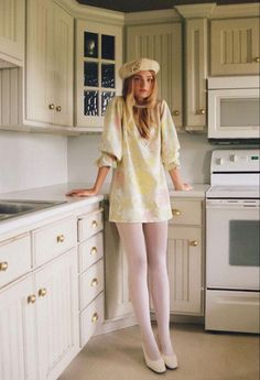 Woman in a floral dress, beret, and white tights standing in a kitchen