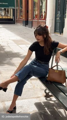 Woman with long hair and bangs sitting on a bench on a sunny street