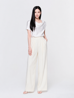 Woman with long black hair wearing a white blouse and wide leg pants in a studio