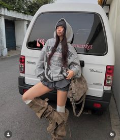 Woman in a grey hoodie, beanie, and oversized boots leaning on a white van