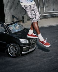 Person in camo shorts and red sneakers standing on a toy car