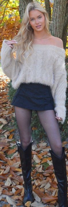 Blonde woman in an off-shoulder sweater and black skirt standing outdoors