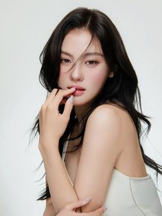 Woman with long black hair and a white top posing against a white background