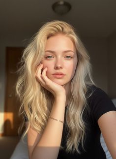 Blonde woman with blue eyes resting her chin on her hand, bathed in soft indoor light