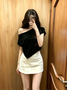 Woman in a black off-shoulder top and white mini skirt taking a mirror selfie