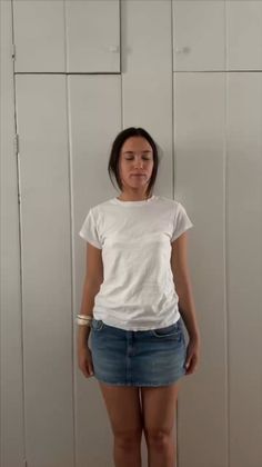 Woman in a white t-shirt and denim skirt standing indoors with closed eyes