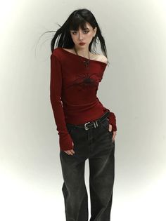 Woman with long black hair and dark makeup wearing a red off-shoulder top and black jeans