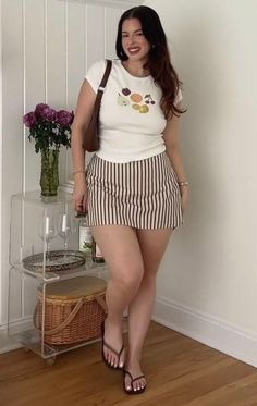 Woman with long dark hair wearing a striped skirt and white t-shirt indoors