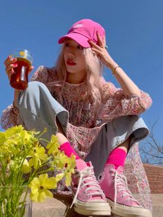 Woman in a pink cap and floral dress holding a drink outdoors