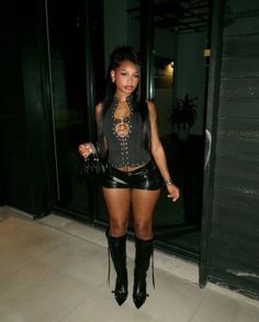Woman in a black lace-up top and leather shorts with knee-high boots