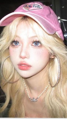 Blonde woman with blue eyes wearing a pink hat and pearl necklace