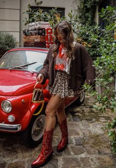 Woman in a leopard print skirt and red cowboy boots next to a red car with stacked luggage